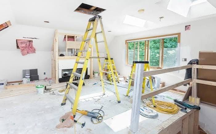 Room mid-renovation with yellow stepladders, an open ceiling hatch, new wall framing and tools on the floor