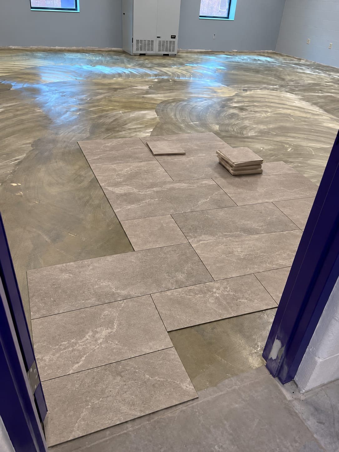 Large gray marble-look porcelain floor tiles being laid in an offset pattern over a glossy prepared subfloor