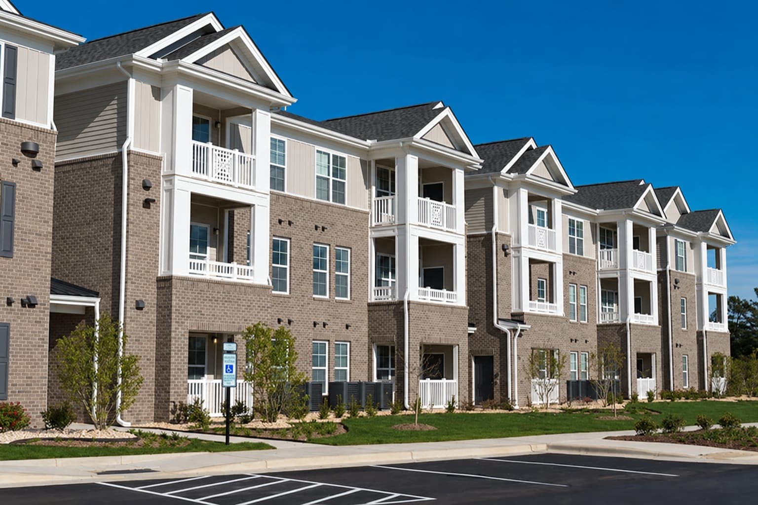 Three-story brick and siding residential buildings with white balconies, new landscaping and a striped parking lot