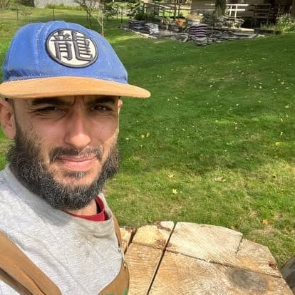 Justin, owner of My Three Rose Facility Management, in a blue cap and work clothes on a lawn