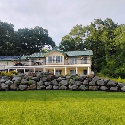 Large boulder retaining wall below a cream two-level house with a green metal roof on an overcast day
