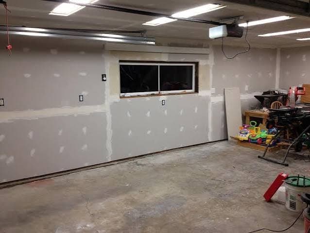 Garage walls covered in new drywall, with joint compound spotted over screws and seams around a wide window