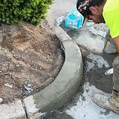 Worker in a hi-vis shirt finishing a freshly poured curved concrete curb around a planting bed