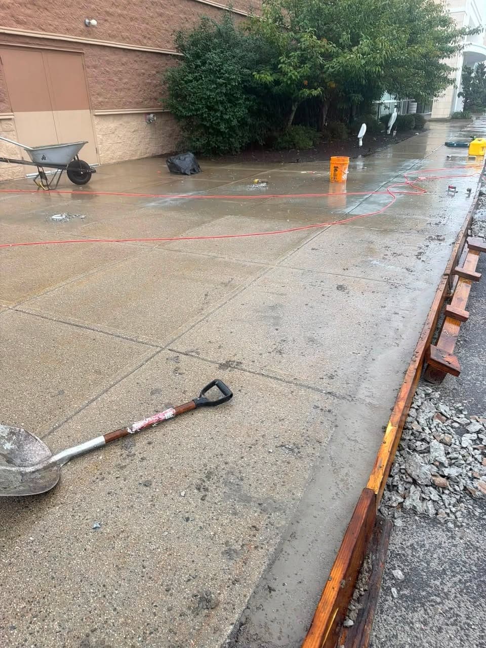 Puddled concrete walkway beside a commercial building, with new concrete poured along its edge against wood forms