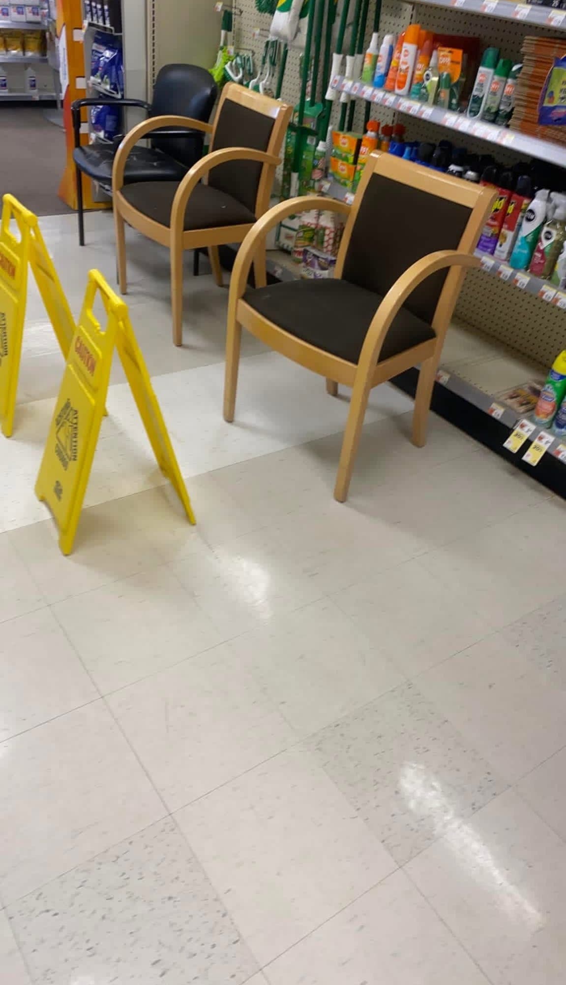 Glossy white vinyl tile floor in a retail store aisle with yellow wet-floor signs beside wood-framed chairs