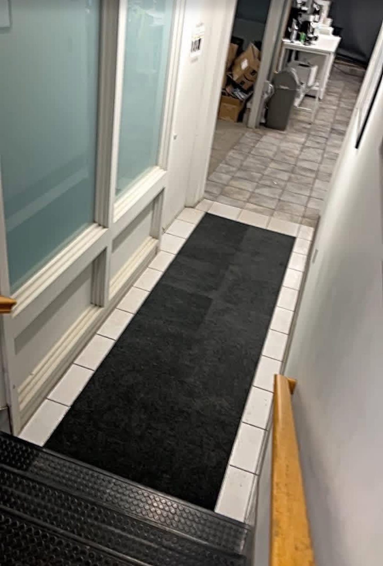 Stair landing with a black carpet inset framed by white ceramic tile, beside frosted glass office windows