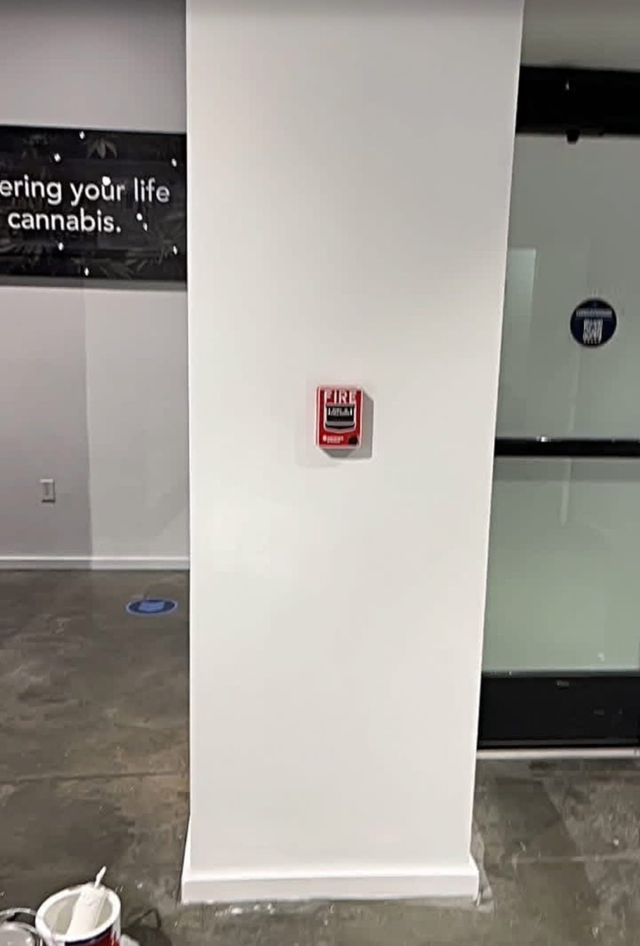 Freshly painted white column with a red fire alarm pull station and an open paint can on the concrete floor