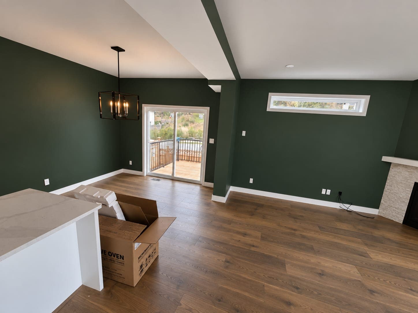 Open living and dining area painted dark green with white trim, a black lantern chandelier and sliding door to a deck