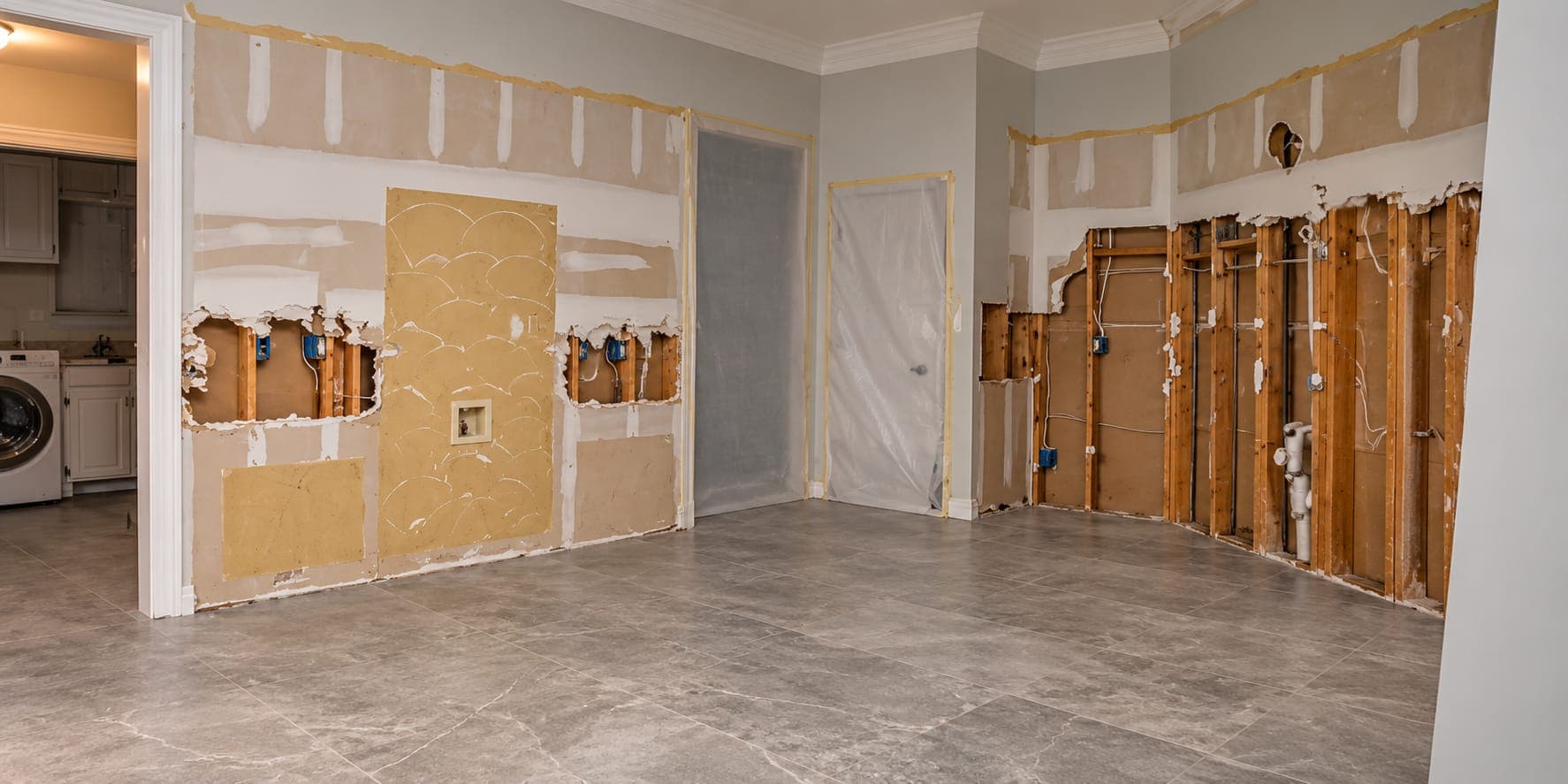 Room remodel with drywall cut away to expose studs, wiring and drain pipes, and doorways sealed in plastic sheeting