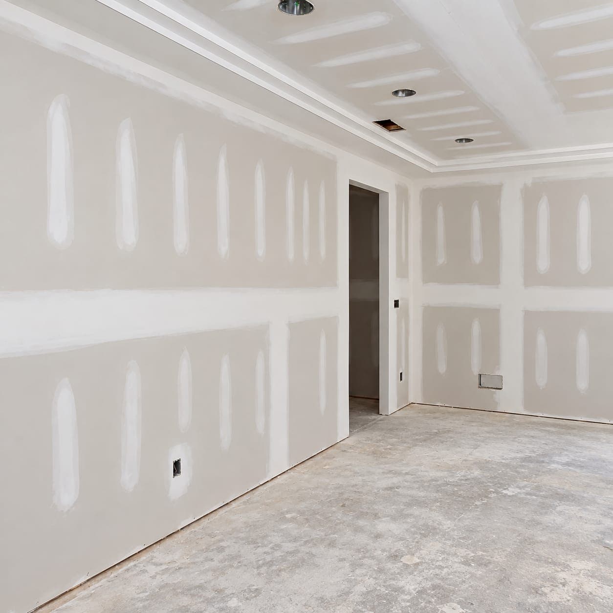 New drywall with taped seams and mudded screw lines in an unfinished room with a tray ceiling and bare concrete floor