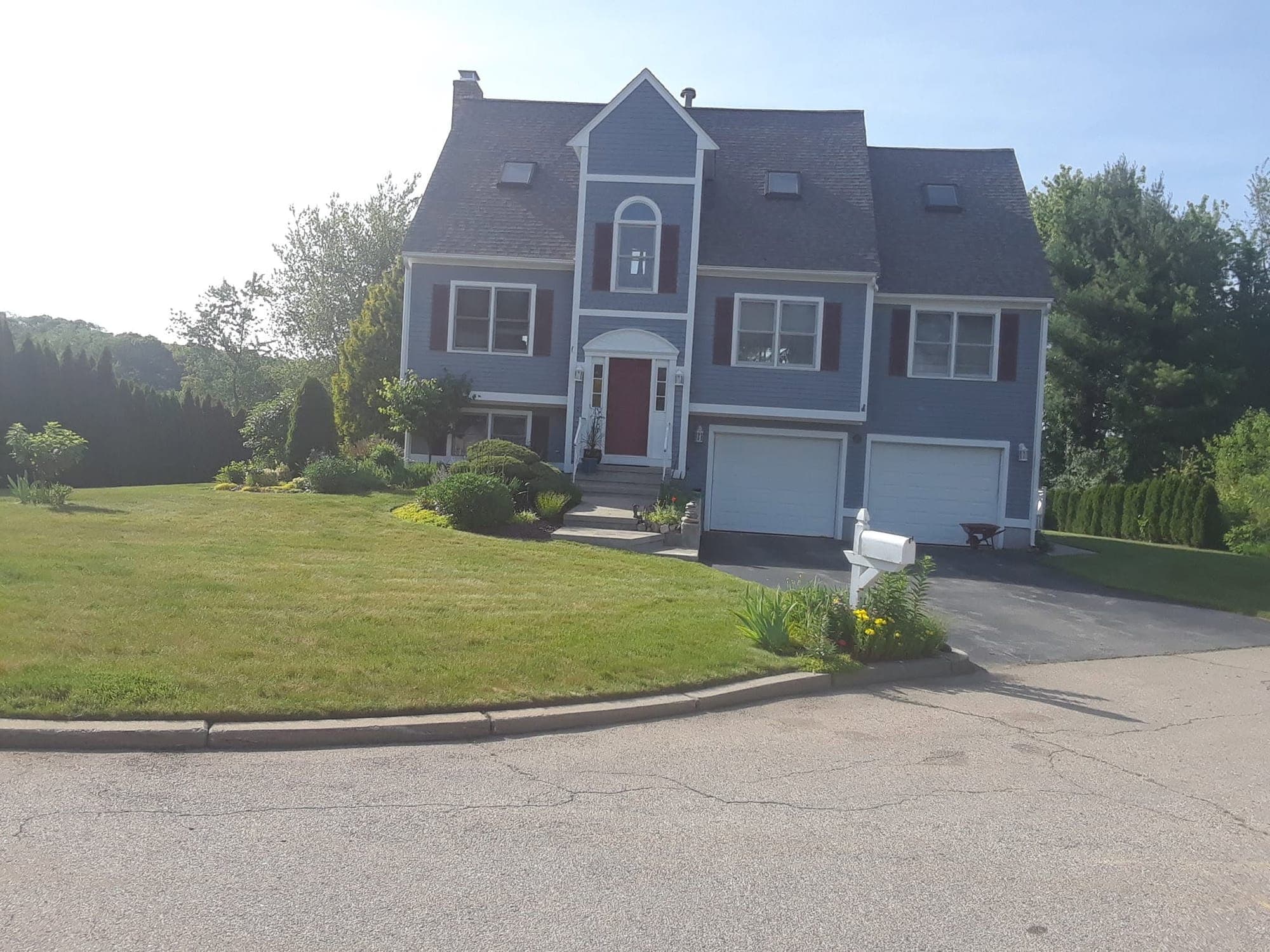 Blue-gray two-story home with red shutters, a black asphalt driveway, two-car garage and mowed front lawn