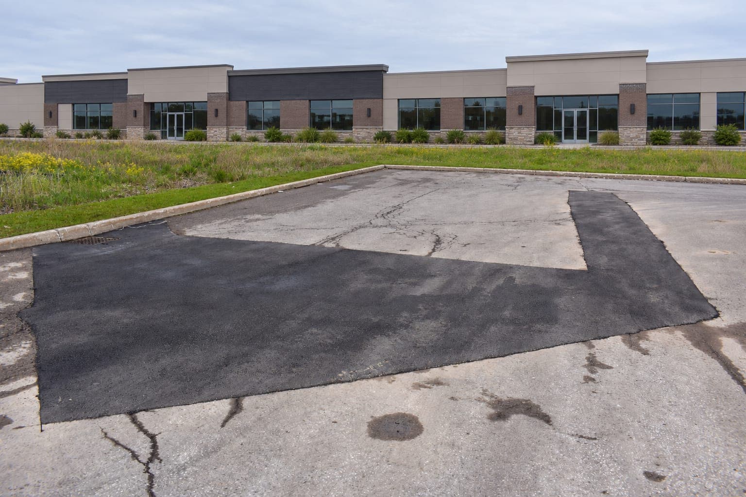Large fresh asphalt patch in a cracked parking lot in front of a single-story commercial building