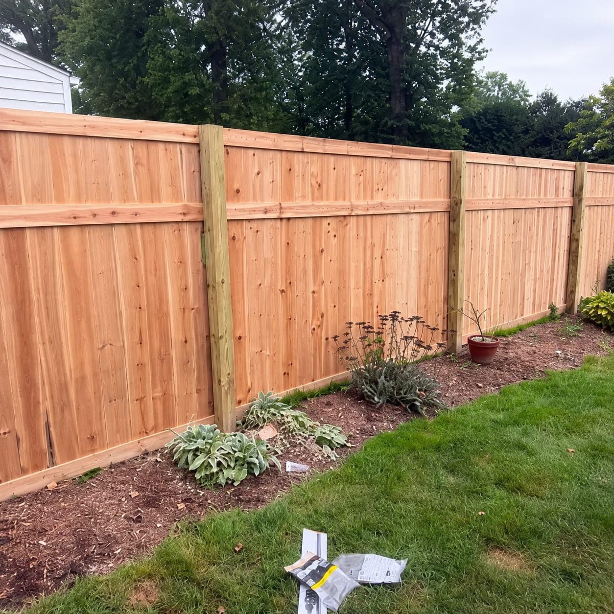 New cedar board privacy fence with pressure-treated posts and a mid rail along a mulched garden bed and green lawn