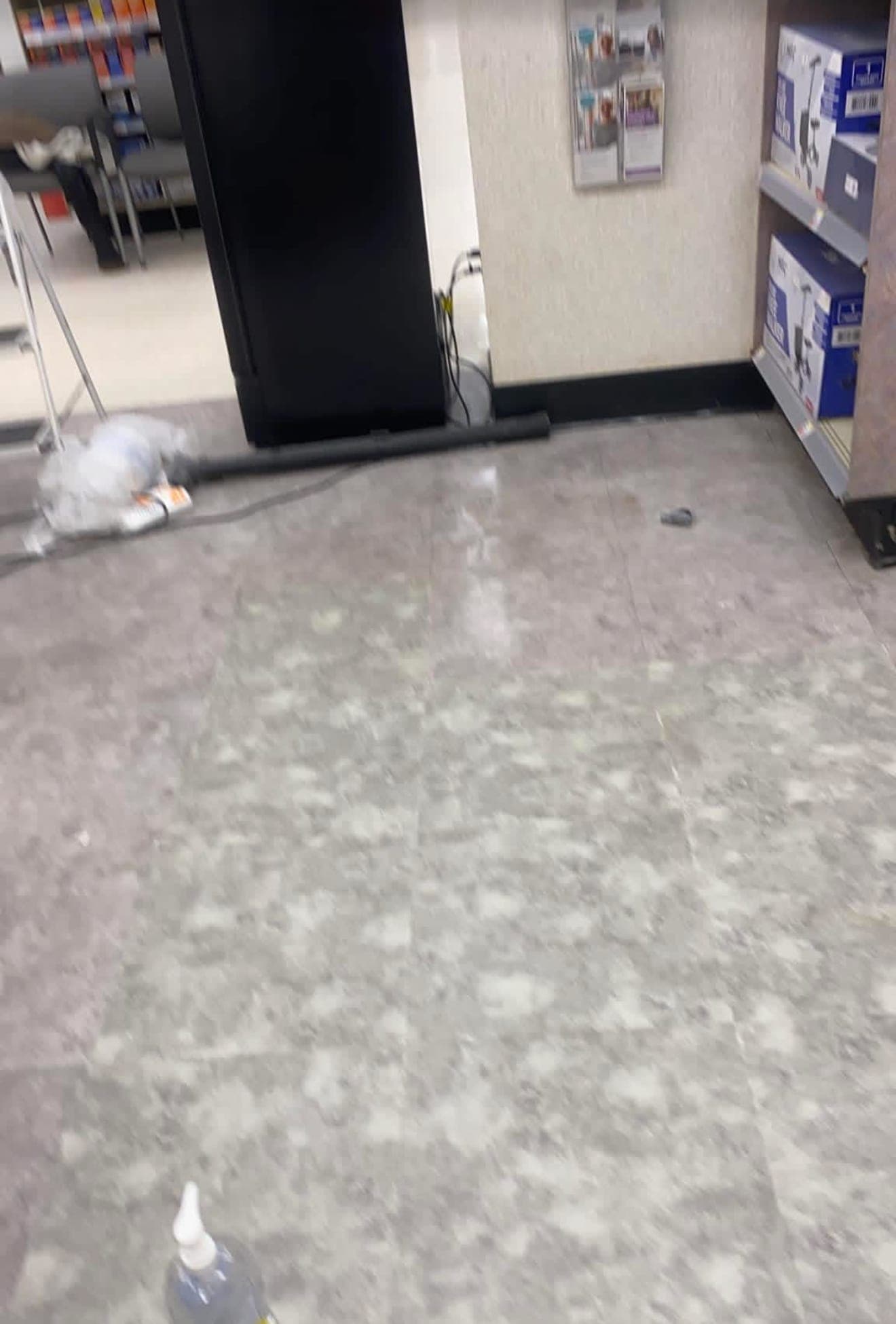Gray vinyl tile floor with patchy white residue in a store aisle, near a stepladder and shelves of boxed knee scooters